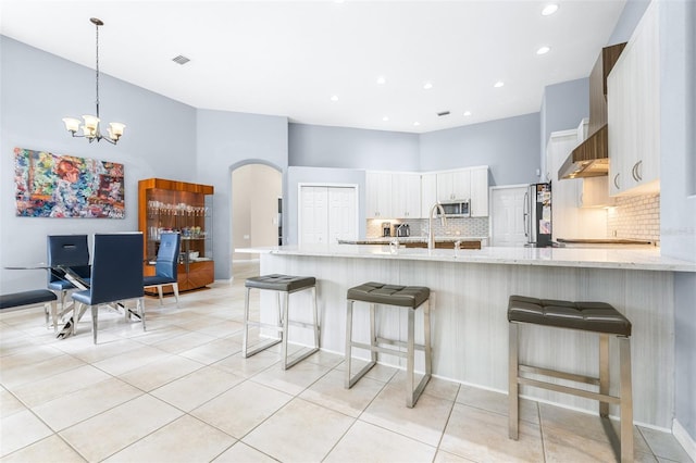 kitchen featuring white cabinetry, backsplash, kitchen peninsula, a towering ceiling, and appliances with stainless steel finishes