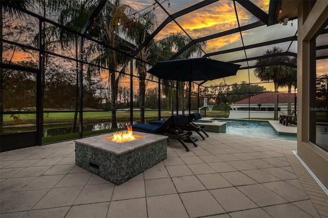 patio terrace at dusk featuring a lanai, a swimming pool with hot tub, a water view, and an outdoor fire pit