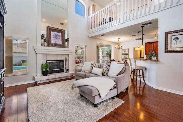 living room with a towering ceiling, a textured ceiling, an inviting chandelier, a fireplace, and dark hardwood / wood-style floors