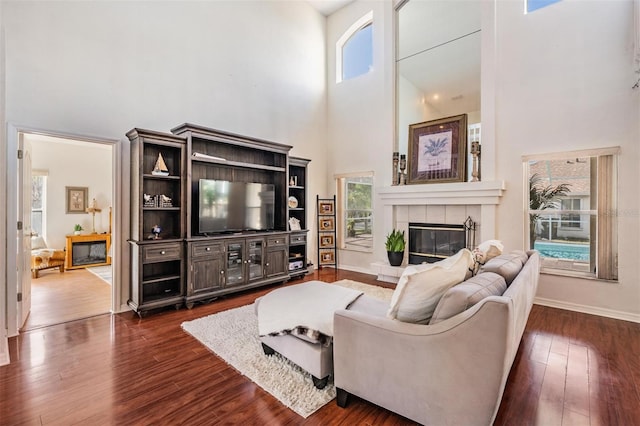 living room with dark hardwood / wood-style flooring, a high ceiling, and a tiled fireplace