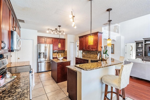 kitchen featuring stone counters, sink, appliances with stainless steel finishes, tasteful backsplash, and decorative light fixtures