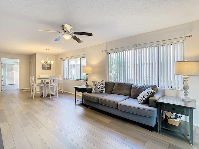 living room featuring wood-type flooring, ceiling fan with notable chandelier, and a textured ceiling