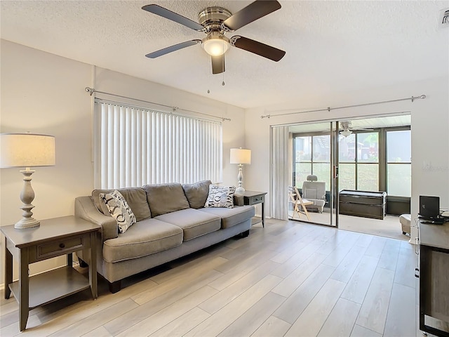 living room with a textured ceiling, light wood-type flooring, and ceiling fan