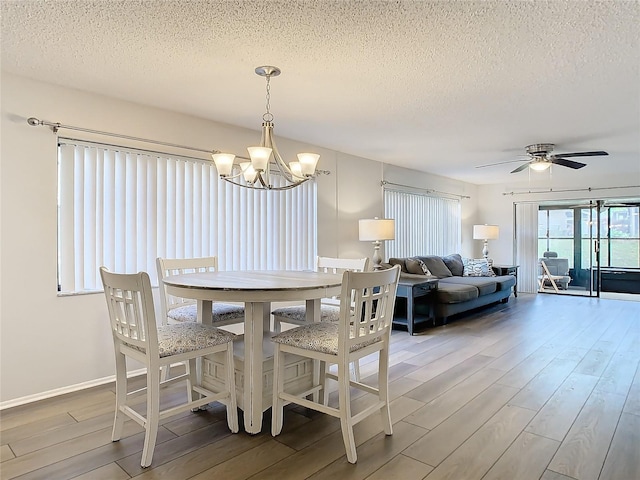 dining space with a textured ceiling, wood-type flooring, and ceiling fan with notable chandelier