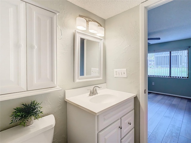 bathroom featuring ceiling fan, wood-type flooring, a textured ceiling, toilet, and vanity