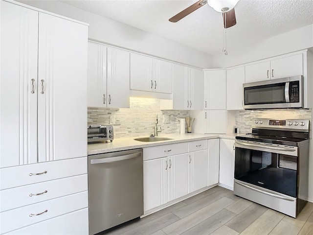 kitchen featuring white cabinets, sink, light hardwood / wood-style flooring, a textured ceiling, and appliances with stainless steel finishes