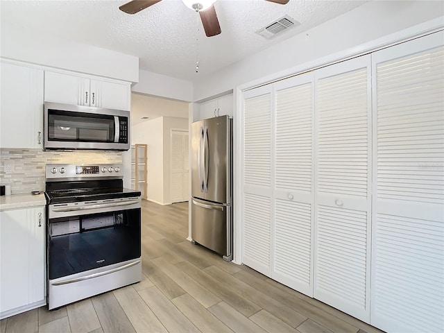 kitchen featuring white cabinetry, backsplash, a textured ceiling, appliances with stainless steel finishes, and light wood-type flooring