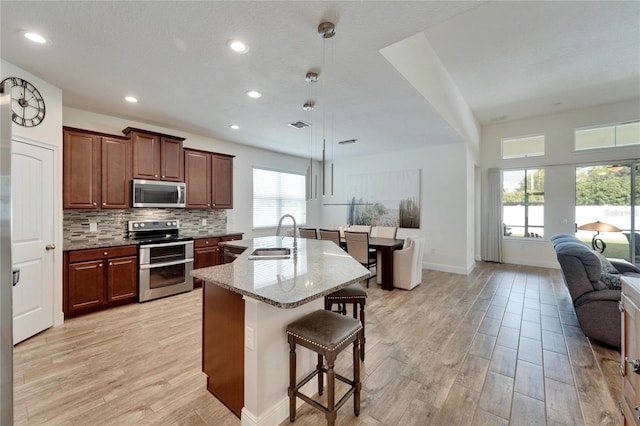 kitchen featuring sink, hanging light fixtures, a kitchen bar, a kitchen island with sink, and appliances with stainless steel finishes