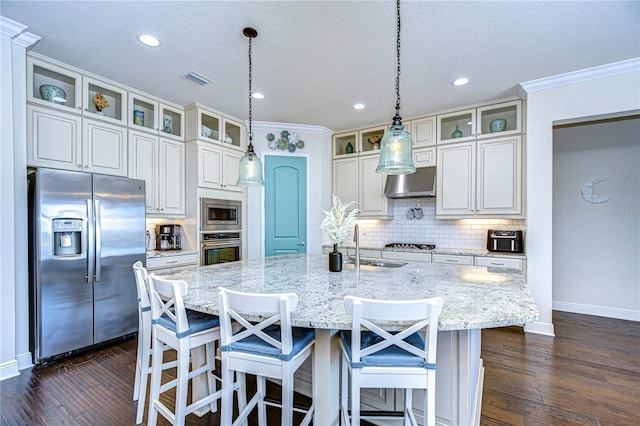 kitchen featuring light stone countertops, pendant lighting, a center island with sink, appliances with stainless steel finishes, and ornamental molding