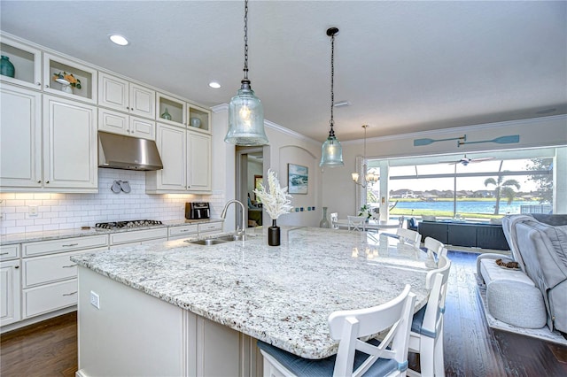 kitchen featuring decorative backsplash, sink, a water view, stainless steel gas stovetop, and an island with sink