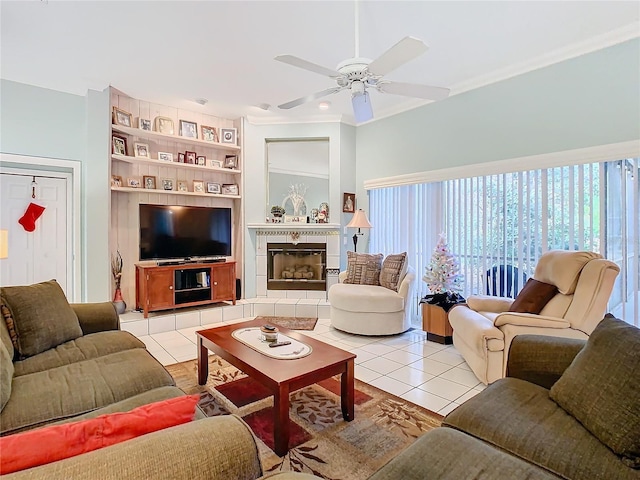 tiled living room featuring built in shelves, ceiling fan, ornamental molding, and a tiled fireplace