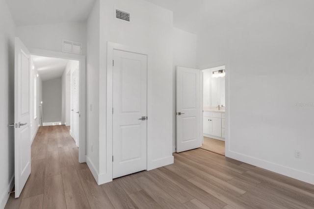 unfurnished bedroom featuring vaulted ceiling, light hardwood / wood-style flooring, and ensuite bath