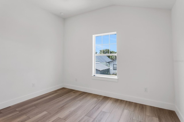 spare room featuring light wood-type flooring and vaulted ceiling