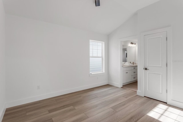 unfurnished bedroom featuring vaulted ceiling, sink, light hardwood / wood-style flooring, and ensuite bath