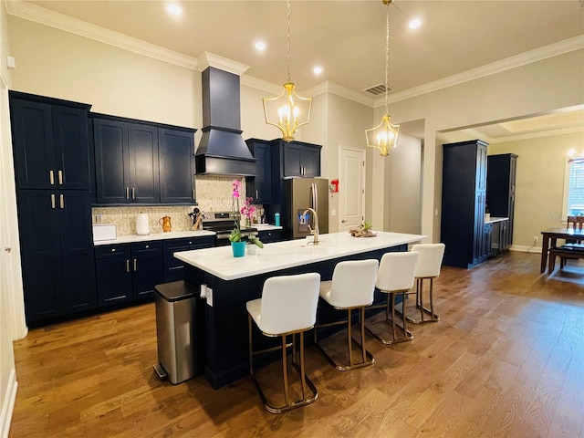 kitchen featuring custom exhaust hood, a center island with sink, a kitchen breakfast bar, light hardwood / wood-style flooring, and stainless steel appliances