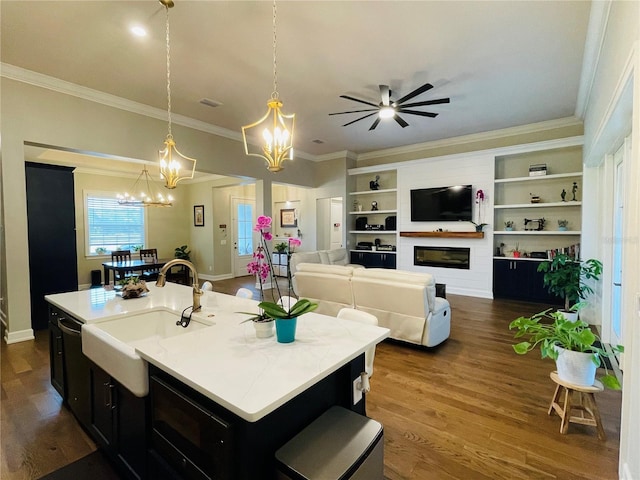 kitchen with a large fireplace, sink, decorative light fixtures, dark hardwood / wood-style floors, and an island with sink