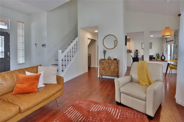 living room with dark hardwood / wood-style flooring, a towering ceiling, and a healthy amount of sunlight