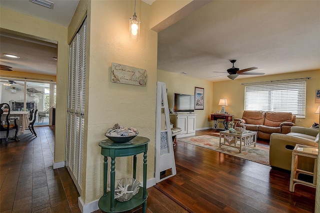 living area with a healthy amount of sunlight, dark wood-style floors, ceiling fan, and baseboards