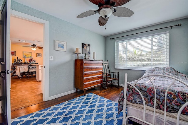 bedroom featuring ceiling fan, a textured wall, baseboards, and wood finished floors