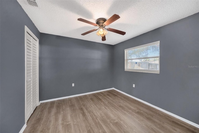 empty room with ceiling fan, wood-type flooring, and a textured ceiling