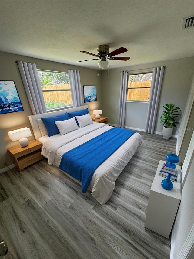 bedroom featuring ceiling fan, wood-type flooring, and multiple windows