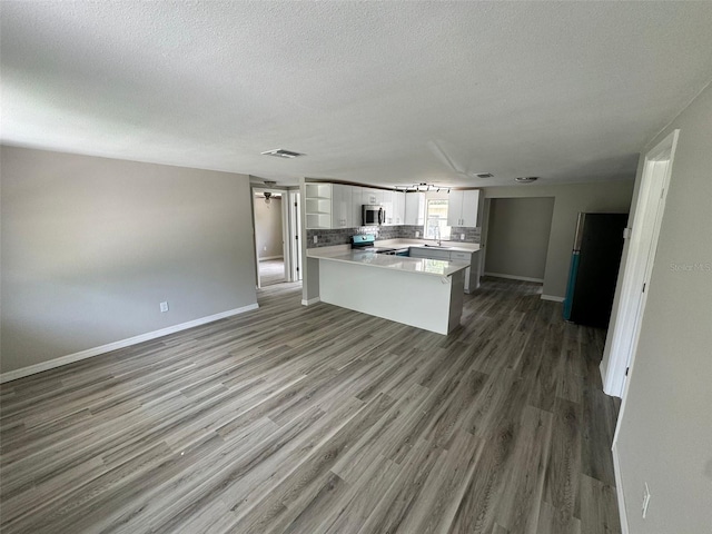 kitchen with hardwood / wood-style floors, a textured ceiling, a kitchen island, white cabinetry, and stainless steel appliances