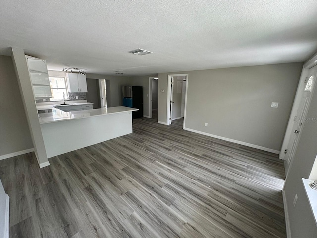 kitchen with hardwood / wood-style flooring, black fridge, white cabinetry, and a textured ceiling