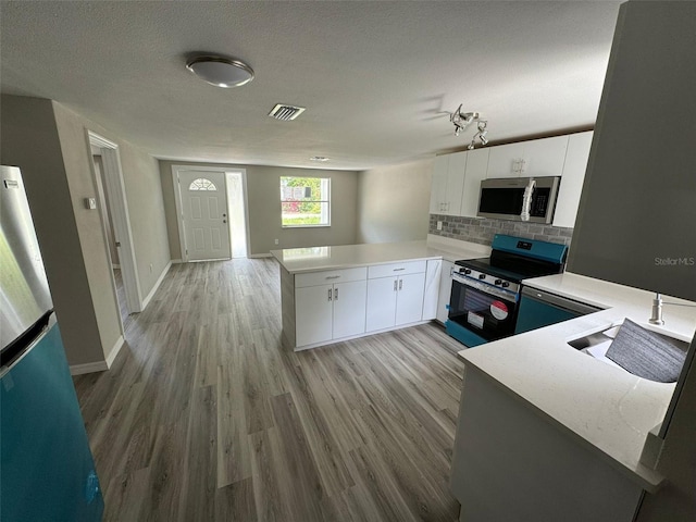 kitchen with kitchen peninsula, stainless steel appliances, white cabinetry, and light hardwood / wood-style floors