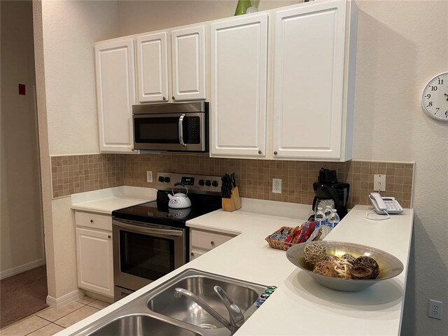 kitchen featuring decorative backsplash, light tile patterned floors, stainless steel appliances, and white cabinetry