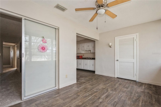 unfurnished room featuring a textured ceiling, ceiling fan, dark wood-type flooring, and sink