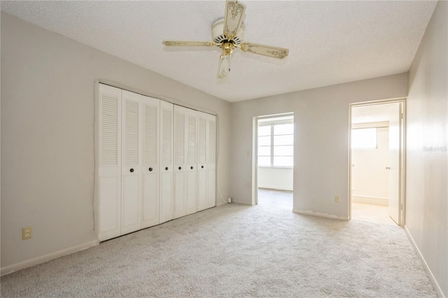 unfurnished bedroom with ceiling fan, a closet, light colored carpet, and a textured ceiling