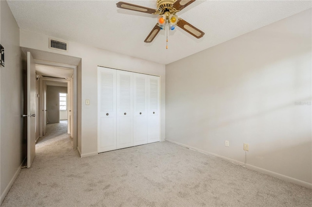 unfurnished bedroom with ceiling fan, a closet, light carpet, and a textured ceiling