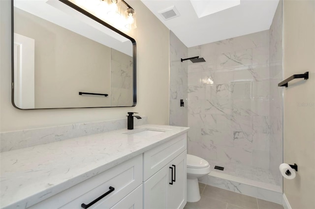 bathroom with a skylight, tile patterned floors, a tile shower, vanity, and toilet