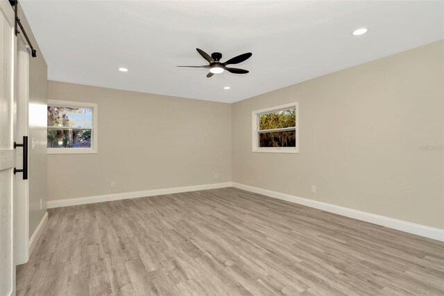 spare room featuring ceiling fan, a barn door, and light hardwood / wood-style flooring