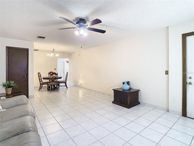 living room featuring ceiling fan with notable chandelier, light tile patterned floors, and a textured ceiling