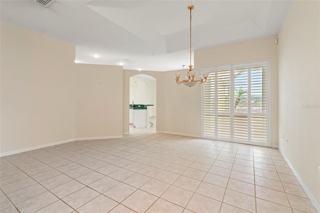 empty room featuring light tile patterned floors, a tray ceiling, and a notable chandelier