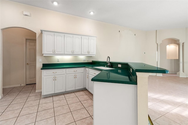 kitchen featuring kitchen peninsula, light tile patterned floors, white cabinetry, and sink