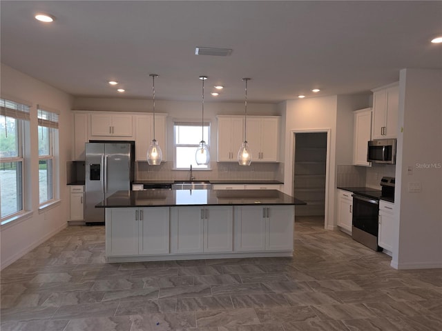 kitchen with backsplash, hanging light fixtures, appliances with stainless steel finishes, a kitchen island, and white cabinetry