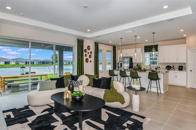 living room featuring light tile patterned floors, a water view, and a raised ceiling