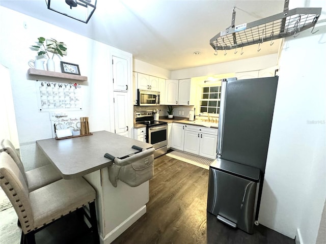 kitchen with dark wood-type flooring, appliances with stainless steel finishes, white cabinetry, a kitchen bar, and kitchen peninsula