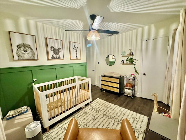 bedroom featuring ceiling fan, dark hardwood / wood-style floors, and a crib