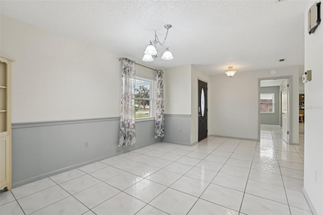 unfurnished room with a notable chandelier, light tile patterned flooring, and a textured ceiling