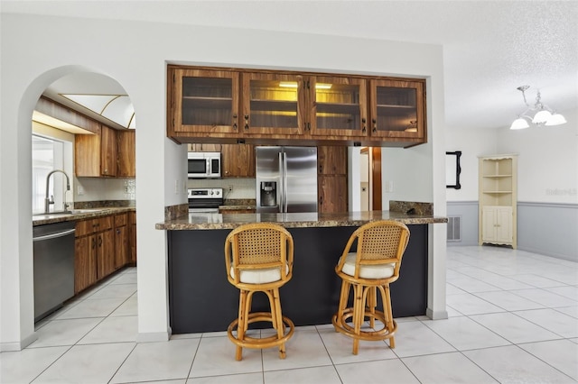 kitchen featuring sink, a textured ceiling, kitchen peninsula, stainless steel appliances, and a chandelier