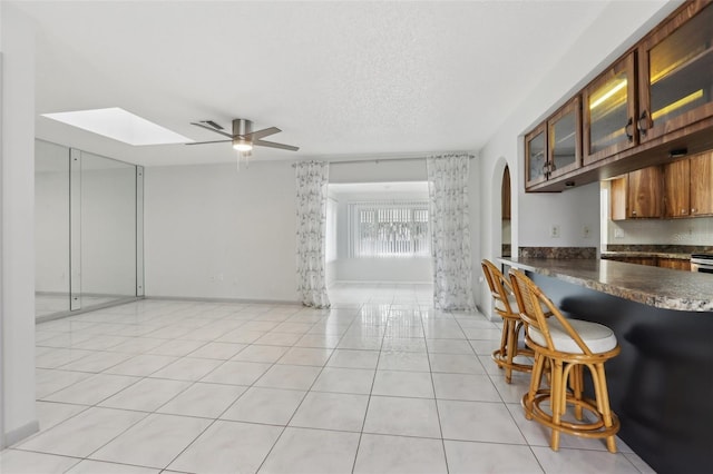 kitchen featuring a kitchen bar, a skylight, a textured ceiling, ceiling fan, and light tile patterned floors