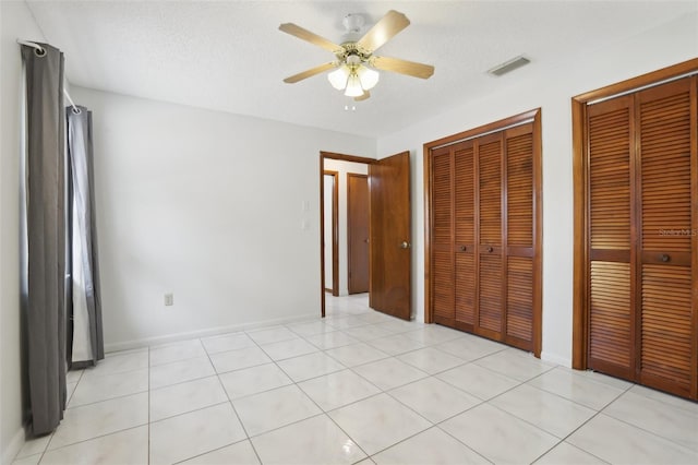 unfurnished bedroom with ceiling fan, light tile patterned floors, a textured ceiling, and multiple closets