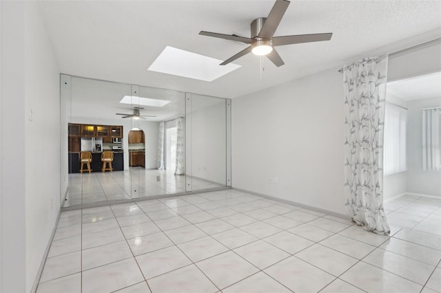 unfurnished room with light tile patterned floors, a textured ceiling, a skylight, and ceiling fan