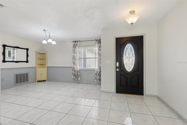 tiled foyer featuring a textured ceiling and a notable chandelier