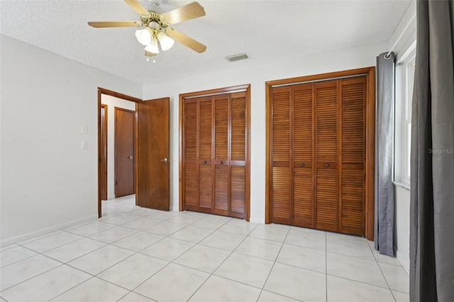 unfurnished bedroom with light tile patterned floors, a textured ceiling, two closets, and ceiling fan