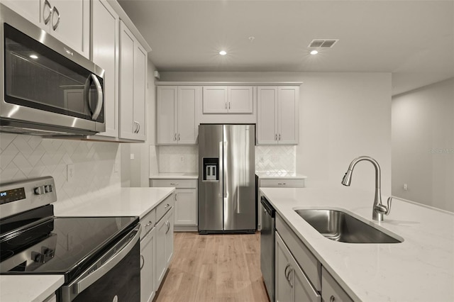 kitchen with sink, white cabinetry, light wood-type flooring, appliances with stainless steel finishes, and light stone countertops