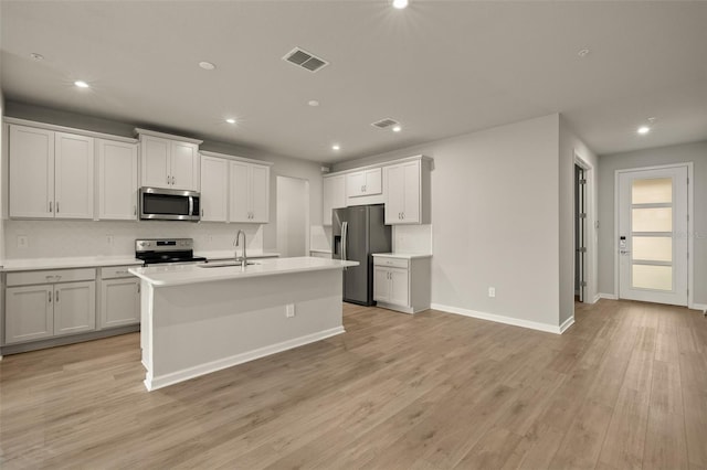 kitchen featuring sink, white cabinets, a kitchen island with sink, stainless steel appliances, and light wood-type flooring